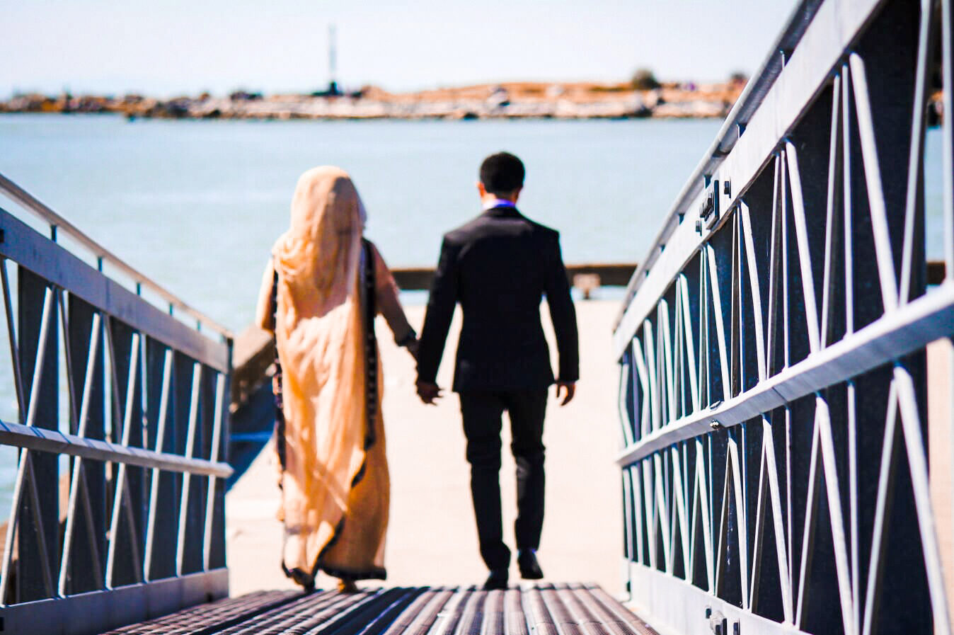 Bride and groom walking hand in hand toward the water